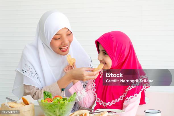 Muslim Mother And Her Daughter Are Eating Cookies Together With A Bowl Of Vegetable Salad On White Background Stock Photo - Download Image Now
