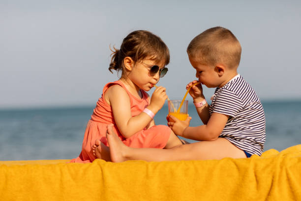 istock Happy kids drinking juice together on the beach 1156543337