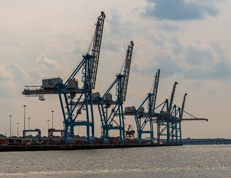 Norfolk, VA, USA -- June 6, 2019. A photo of a row of shipyard cranes set against a bright hazy sky in Port Virginia, Norfolk.