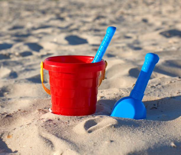 istock red plastic bucket and blue rake, shovel on the sand 1156544801