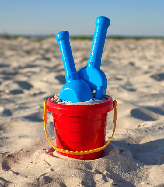 istock red plastic bucket and blue rake, shovel on the sand 1156548146