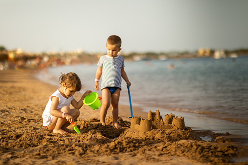 Beautiful children building castle on a sandy beach. Kids enjoying summer sunny day playing with toys