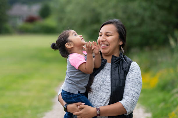 Portrait of a Native American mother and daughter outside A Native American mom holds her toddler-age daughter affectionately while they take a break from walking in the park to smile at each other. indigenous peoples of the americas photos stock pictures, royalty-free photos & images