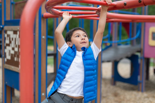 istock Young boy hanging from a play structure at the playground 1156574268