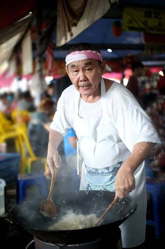 A senior man stir fried vermicelli at morning market stall.