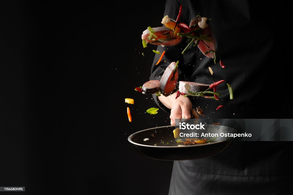 Chef cook fry fish with vegetables on a griddle on a black background. horizontal photo. sea food. healthy food. oriental cuisine, baner Chef Stock Photo