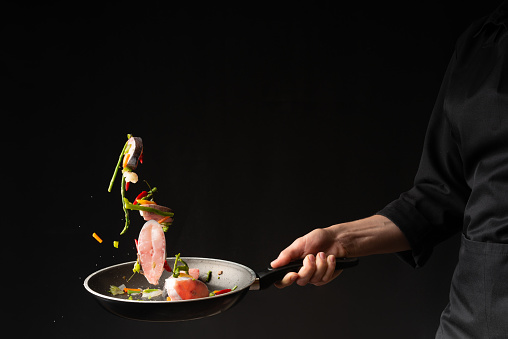 Close-up. Chef cook fry fish with vegetables on a griddle on a black background. horizontal photo. sea food. healthy food. oriental cuisine, baner