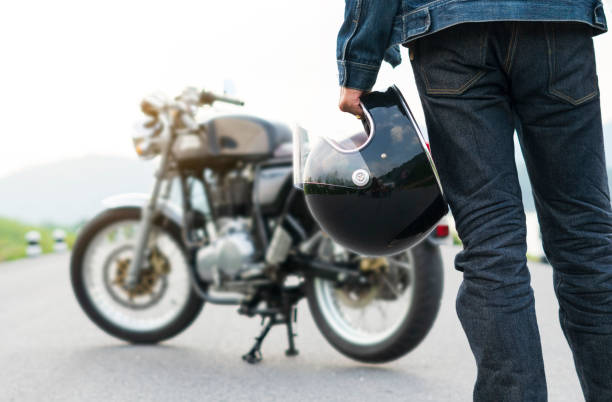 biker fahren in jeans hält einen helm und motorrad unscharf hintergrund. - sturzhelm stock-fotos und bilder