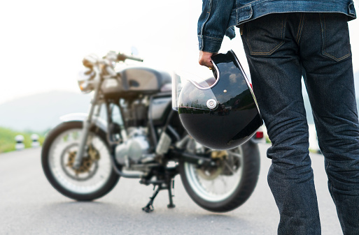 Biker riding in jean is holding a helmet and  motorcycle blur background.