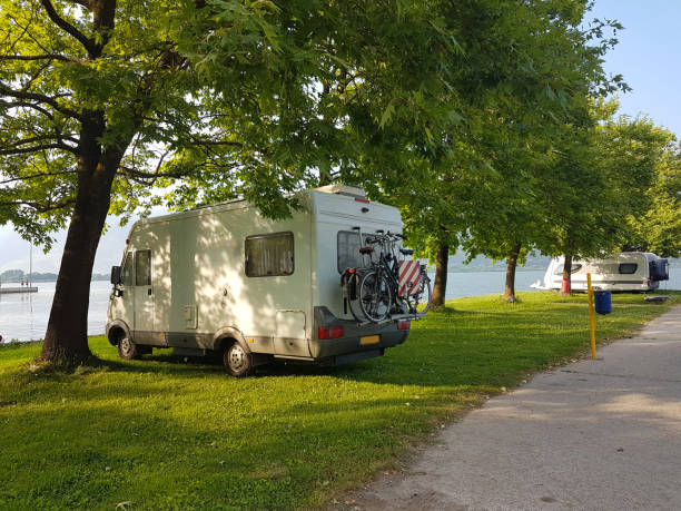 caravane sur l'herbe verte de camping et tress à côté de l'eau du lac - motor home park camping luxury photos et images de collection