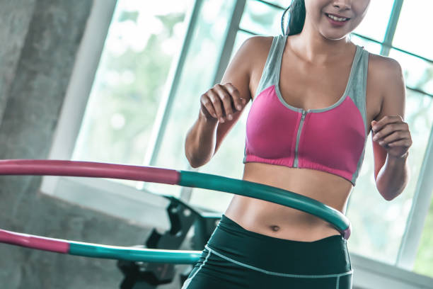 mujeres no reconocidas en ropa deportiva rosa está haciendo ejercicio con hula hoop en el gimnasio para el concepto de estilo de vida saludable - hooping fotografías e imágenes de stock