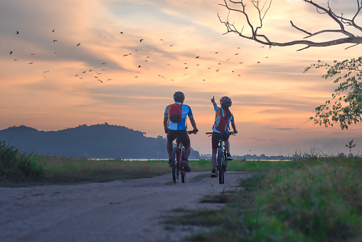couple lover biker cyclist riding enjoyment to the field of meadow lake at sunset, adventure bicycle wild and journey activity