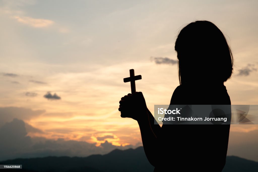 Silhouette of a young girl holding a crucifix to God Morning with beautiful sunrise, Symbol of Faith. Christian life prayer crisis to god. Backgrounds Stock Photo