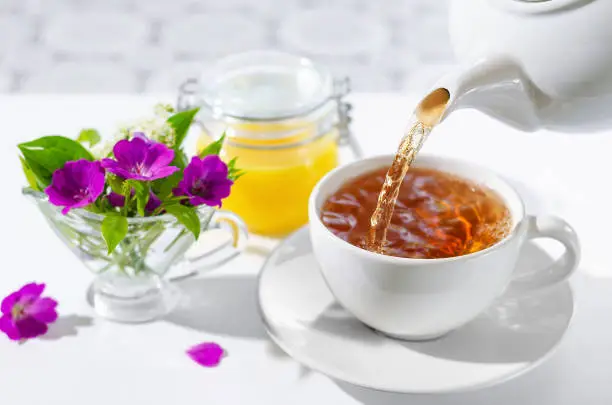 Cup of hot tea with mint and honey on white background. The process of pouring tea. bouquet of flowers and mint leaves.Selective focus.