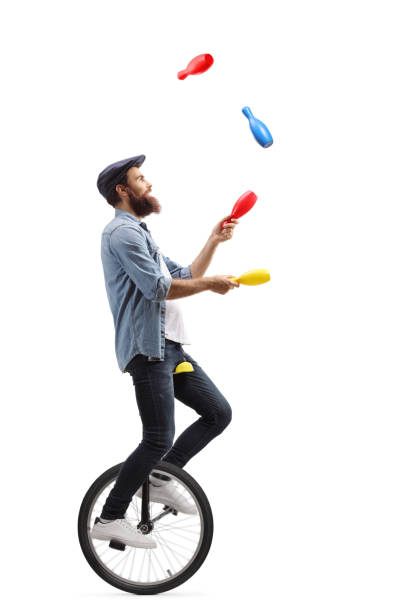 Male juggler on a unicycle juggling with clubs Full length profile shot of a male juggler on a unicycle juggling with clubs isolated on white background juggling stock pictures, royalty-free photos & images