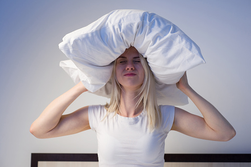 Young woman covering ears with pillow because of noise. - image