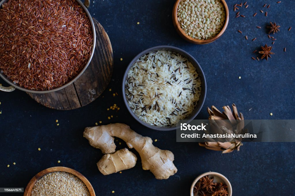 Varios tipos de arroz y granos con especias sobre fondo azul. Arroz integral y arroz silvestre mezclado. - Foto de stock de Abundancia libre de derechos