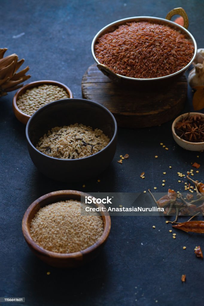 Varios tipos de arroz y granos con especias sobre fondo azul. Arroz integral y arroz silvestre mezclado. - Foto de stock de Abundancia libre de derechos