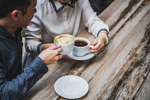 Man drinking cappuccino with friend drinking black coffee at natural wooden table, alternative lifestyle, food and drink, taking a break