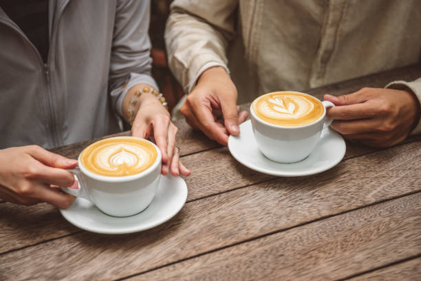 Close up of two people sitting at wooden table holding cups of coffee, hands, romance, dating