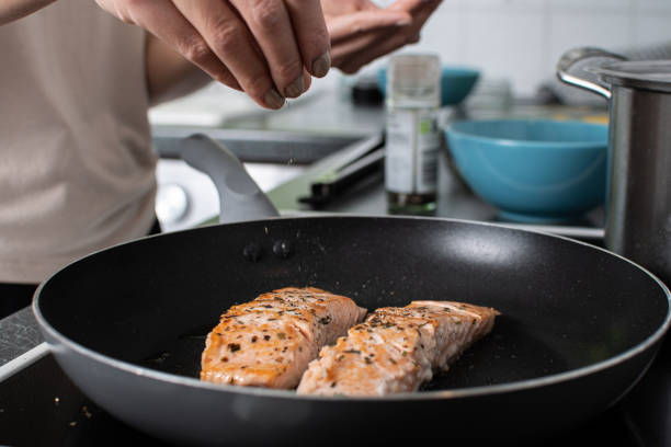 fried salmon cooking on the hob and adding herbs and spices