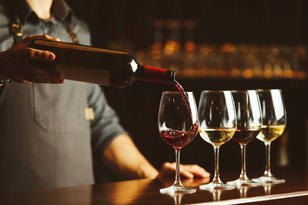 el camarero vierte vino tinto en copas en el mostrador de la barra de madera - wine pour fotografías e imágenes de stock