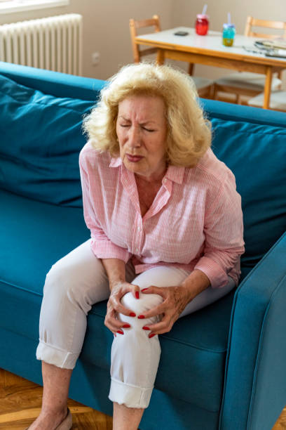 starsza kobieta cierpiąca na ból nóg i uraz kolana siedząca na kanapie. - arthritis senior adult rheumatoid arthritis sadness zdjęcia i obrazy z banku zdjęć