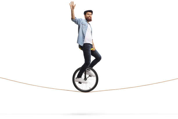 istock Bearded young man riding a unicycle on a rope and waving 1156658458