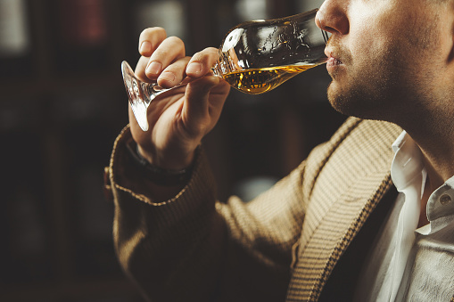 Close-up shot of sommelier tasting whiskey taste on the cellar background. Expert in the field of alcoholic beverages testing drink.