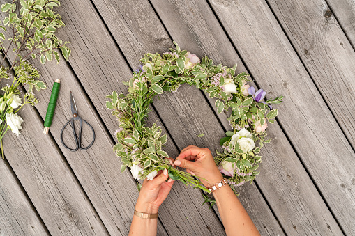 Top down view of a woman in Sweden making floral crown for midsummer celebrations on a summer day. Traditional Swedish wreath.