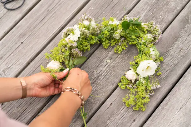 A woman in Sweden is making floral crown for midsummer celebrations on a summer day. Traditional Swedish wreath.