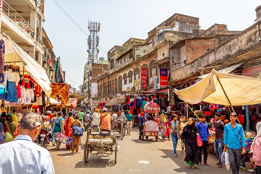 This pic shows  People walking along a busy and crowded street, motorbikes and rickshaws in a dusty street in New Delhi. The  pic is taken in may 2019.