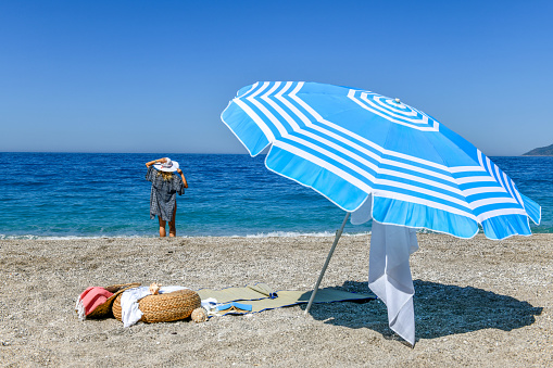 A vibrant colored umbrella resting in the sand surrounded by the tranquil crystal blue waves of the ocean