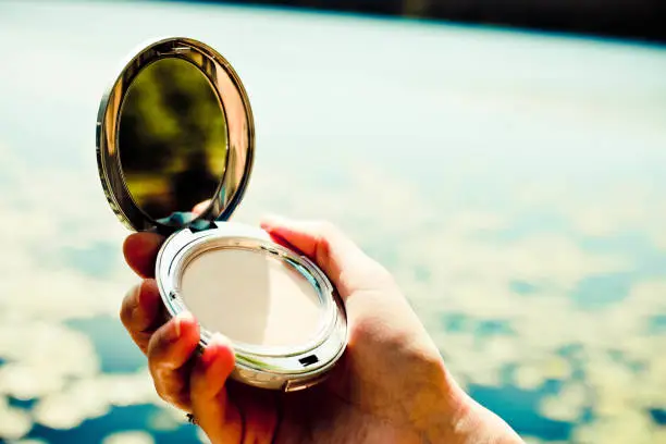 Close up of woman's hand applying face powder on the street. Beautiful blurred background with free space for text.