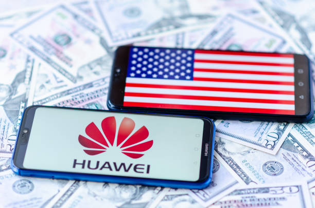 The close up photo of two mobile phones on dollar bills with Chinese HUAWEI logo and American flag. The conceptual editorial photo shows US China trade war. stock photo