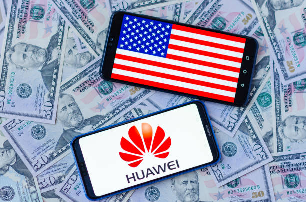 The close up photo of two mobile phones on dollar bills with Chinese HUAWEI logo and American flag. The conceptual editorial photo shows US China trade war. stock photo