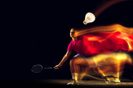 See the target. Little boy playing badminton on black background in mixed light. Young sportsman in action, motion in game with the fire shadows. Concept of sport, movement, healthy lifestyle.