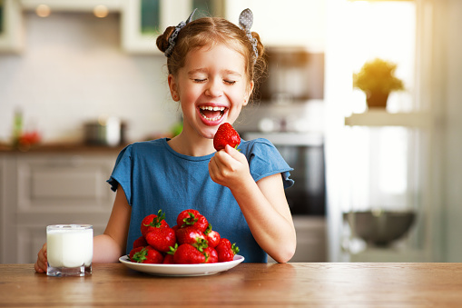 happy child girl eating strawberries with milk at home