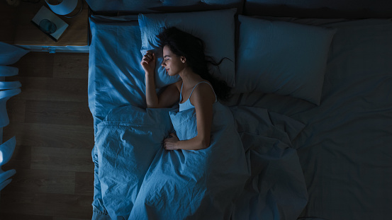 Vista superior de la hermosa mujer joven durmiendo acogedoramente en una cama en su dormitorio en la noche. Colores azules nocturnos con luz de farola débil fría que brilla a través de la ventana. photo