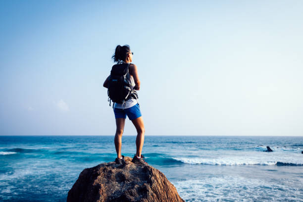 istock Young woman backpacker on seaside rock cliff edge looking down 1156682481
