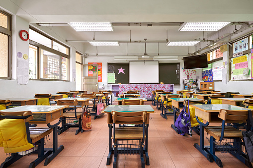 Interior of classroom in elementary school. Row of empty desks are in illuminated room.