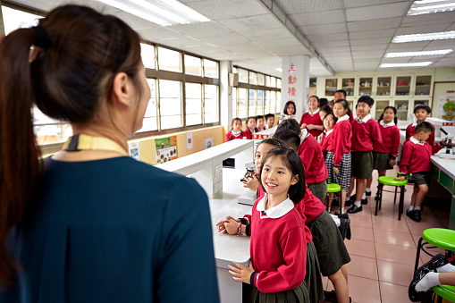 Female professional talking with students. Teacher is teaching pupils in classroom. Schoolkids are wearing uniform.