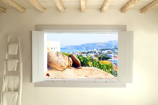 Magical white window offering a beautiful view of the island of Mykonos (Greece) in the Cyclades in the heart of the Aegean Sea.