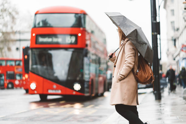 frau wartet auf einem busbahnhof, während doppeldeckerbus nähert - london in the rain stock-fotos und bilder