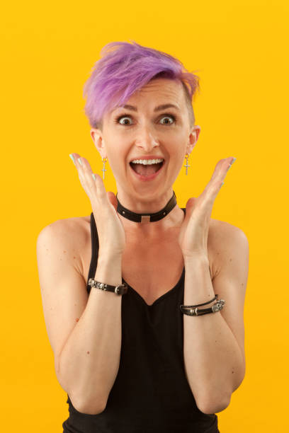 Studio portrait of a 30 year old woman with purple iroquois on a yellow background Studio portrait of a 30 year old woman with purple iroquois on a yellow background purple hair stock pictures, royalty-free photos & images