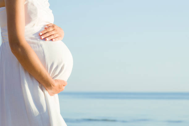 pregnant woman standing at sea beach. sunny day. emotional loving pregnancy time. baby expectation. empty place for lovely, inspiration text, positive quote or cute sayings. big belly close up. - dress human pregnancy young women women imagens e fotografias de stock