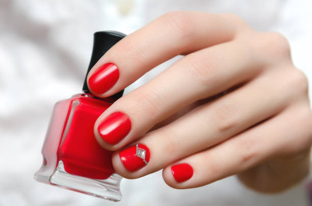 kobieca ręka z czerwonym wzorem paznokci trzymająca butelkę do paznokci - red nail polish zdjęcia i obrazy z banku zdjęć
