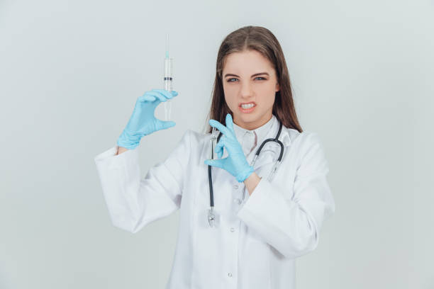 istock Strange female doctor holding syringes, setting teeth, looking crazily. Blurred needles on the forefront. 1156708385