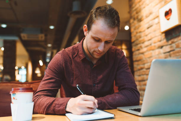 istock Young man working on laptop and taking notes at a cafe 1156709877