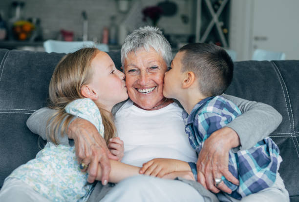 Lovely kids kissing their grandmother Grandmother embracing her cute grandson and granddaughter on the sofa at home. grandchild stock pictures, royalty-free photos & images